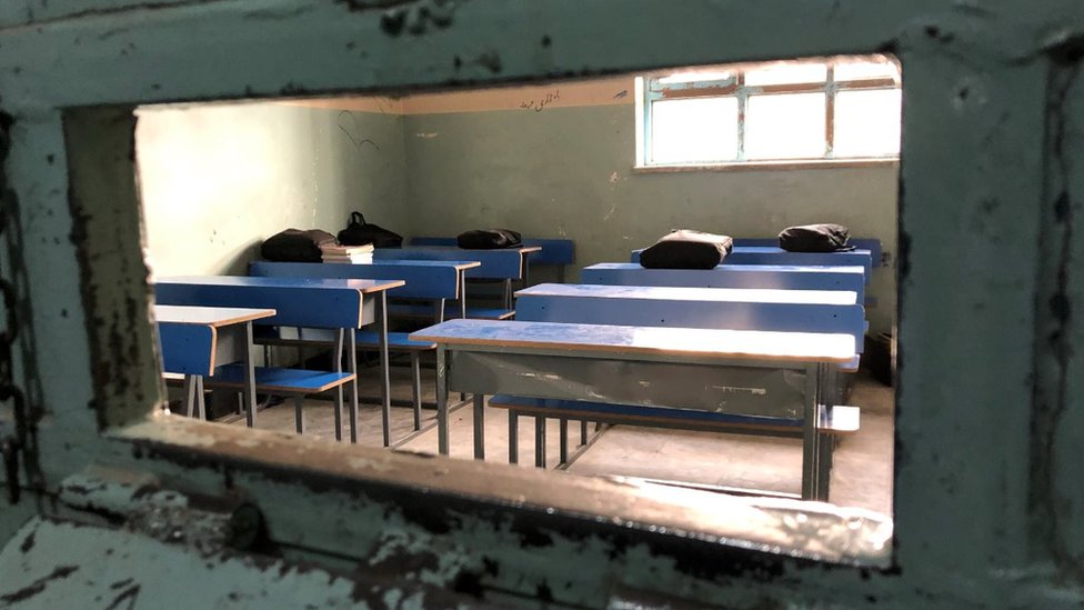 Some blue desks with books on in a classroom