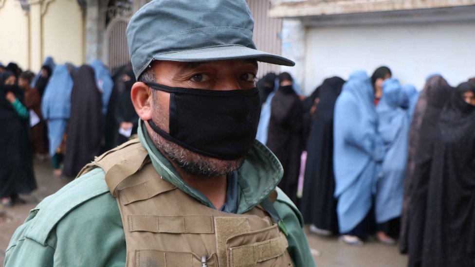 Security force stands guard as women line up to receive free ration distributed by WFP