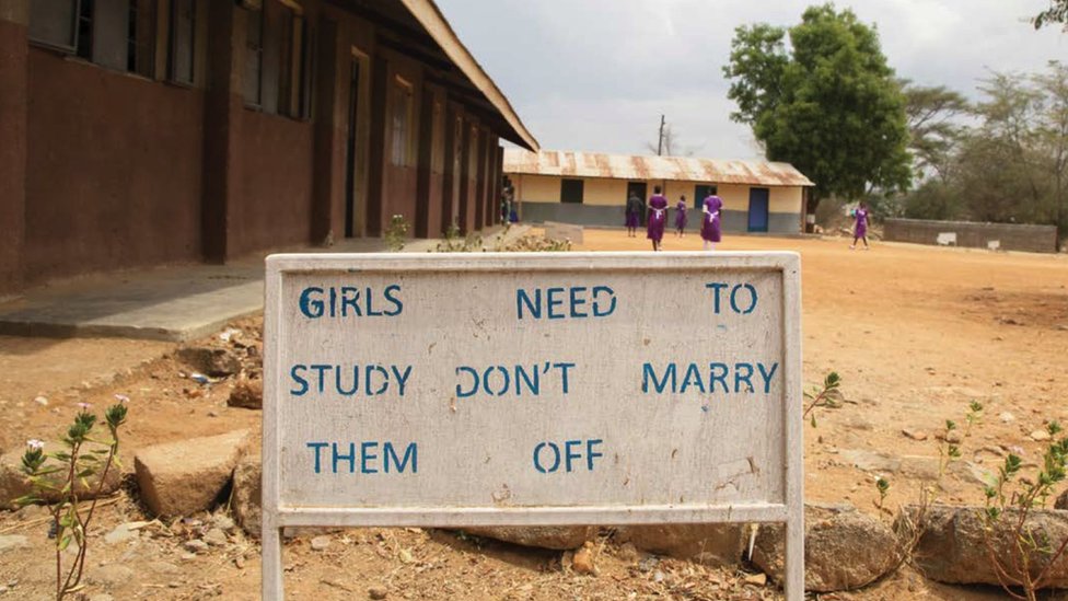 A school playground in Africa - a billboard reads "Girls need to study, don't marry them off"